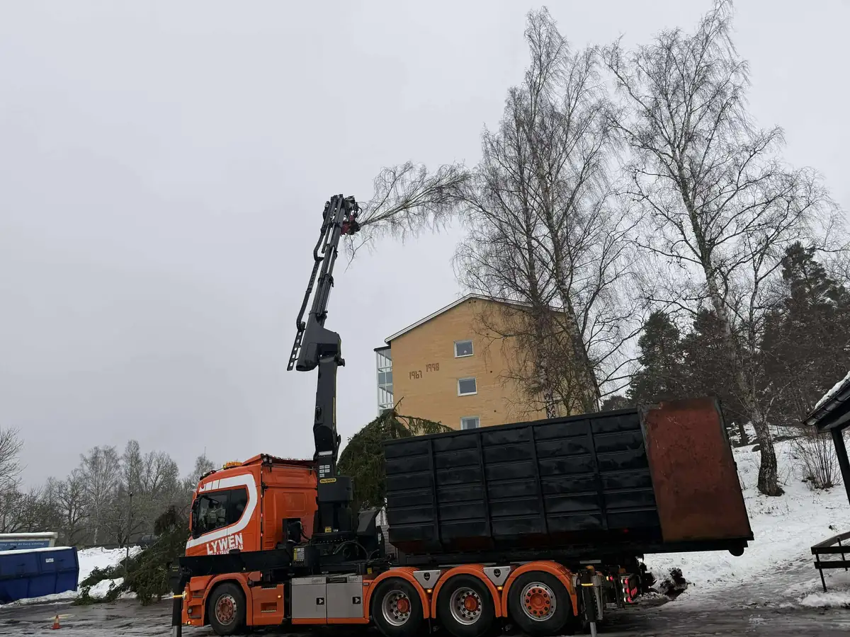 Lywén trädplockning i Östergötland - orange kranbil med lastväxlarflak och kransåg vid bostadsområde